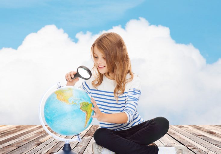 37681040 - education, travel, childhood, geography and school concept - happy little student girl looking at globe with magnifier over blue sky and cloud background